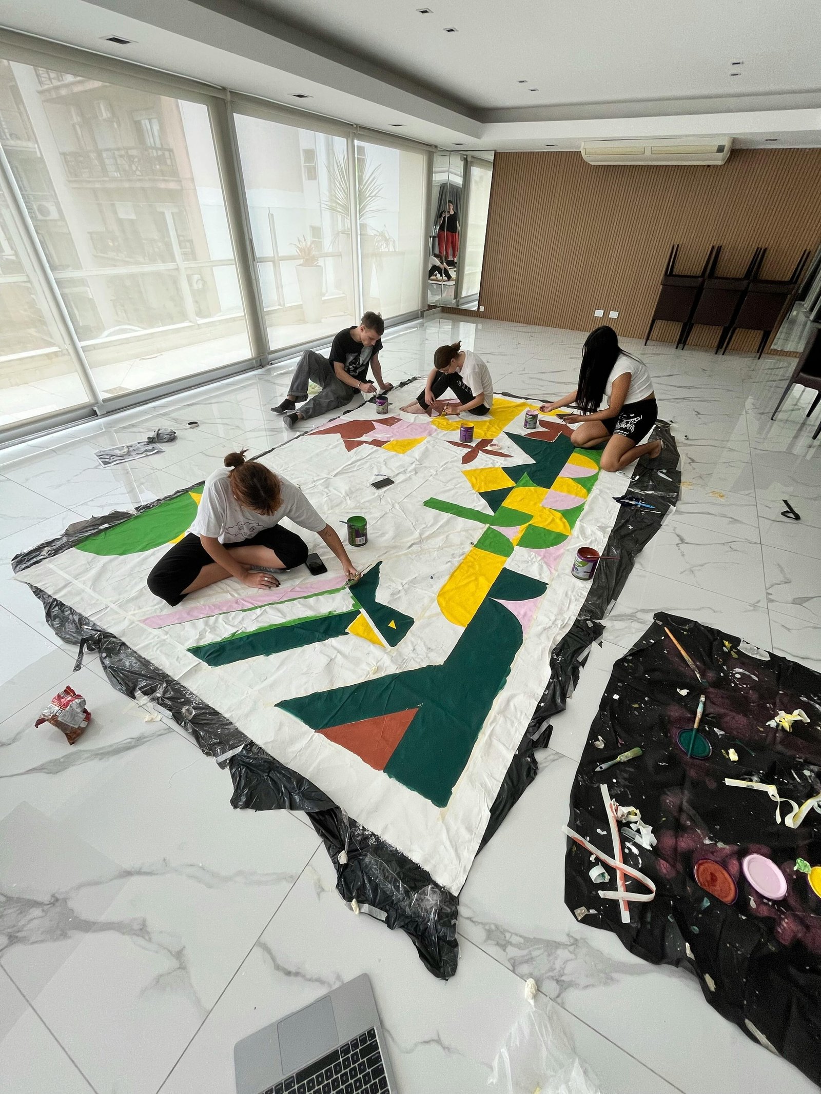 A group of teenagers painting a large abstract canvas together indoors, showcasing teamwork and creativity.